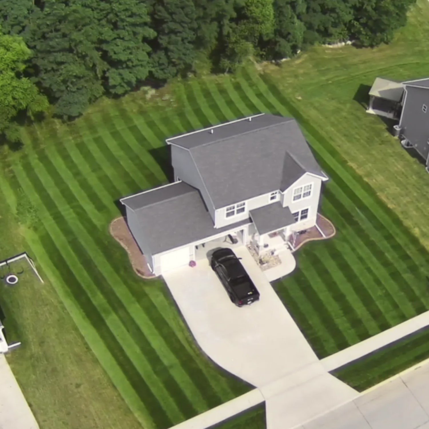 Aerial view of a two-story house with a car in the driveway, surrounded by lush green grass and trees.